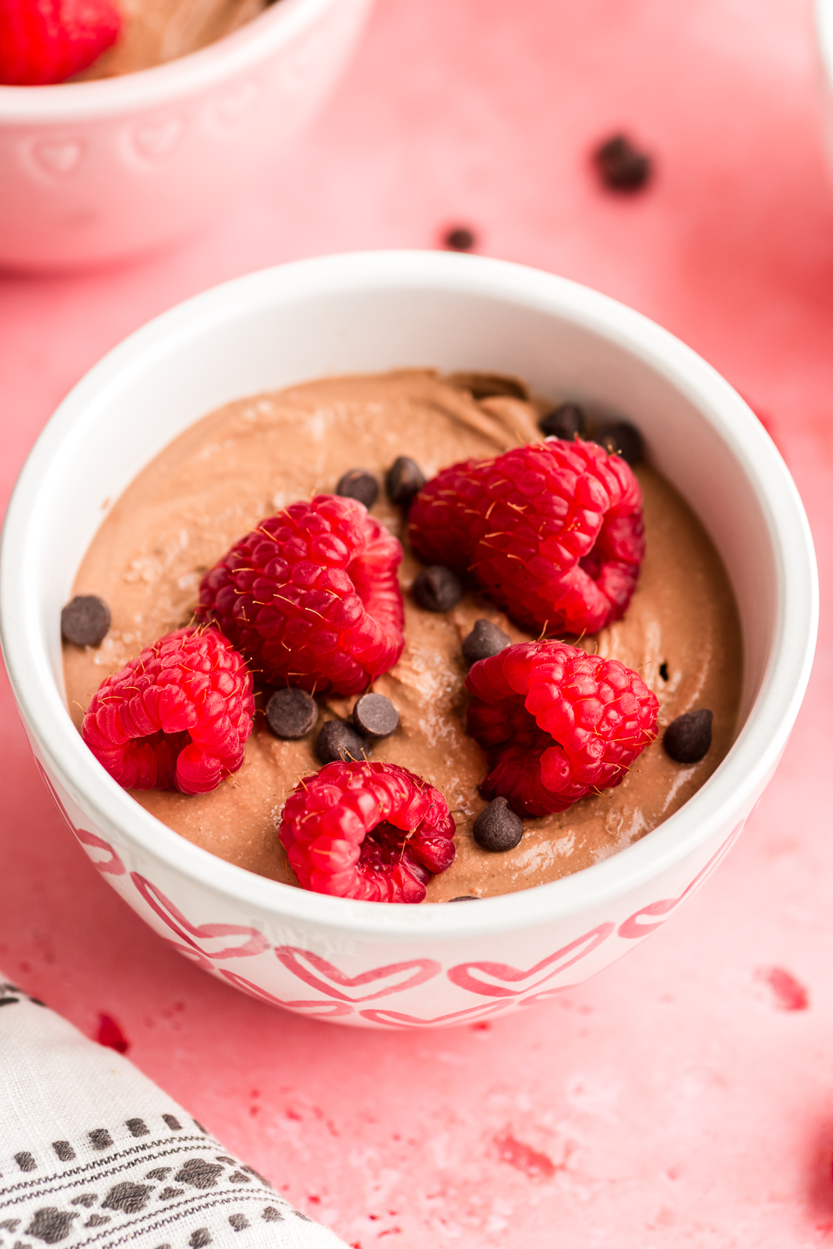 Protein chocolate mousse in a bowl with raspberries and chocolate chips on top.