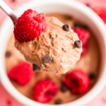 Large spoonful of chocolate cottage cheese mousse being lifted out of a bowl with raspberries on top.