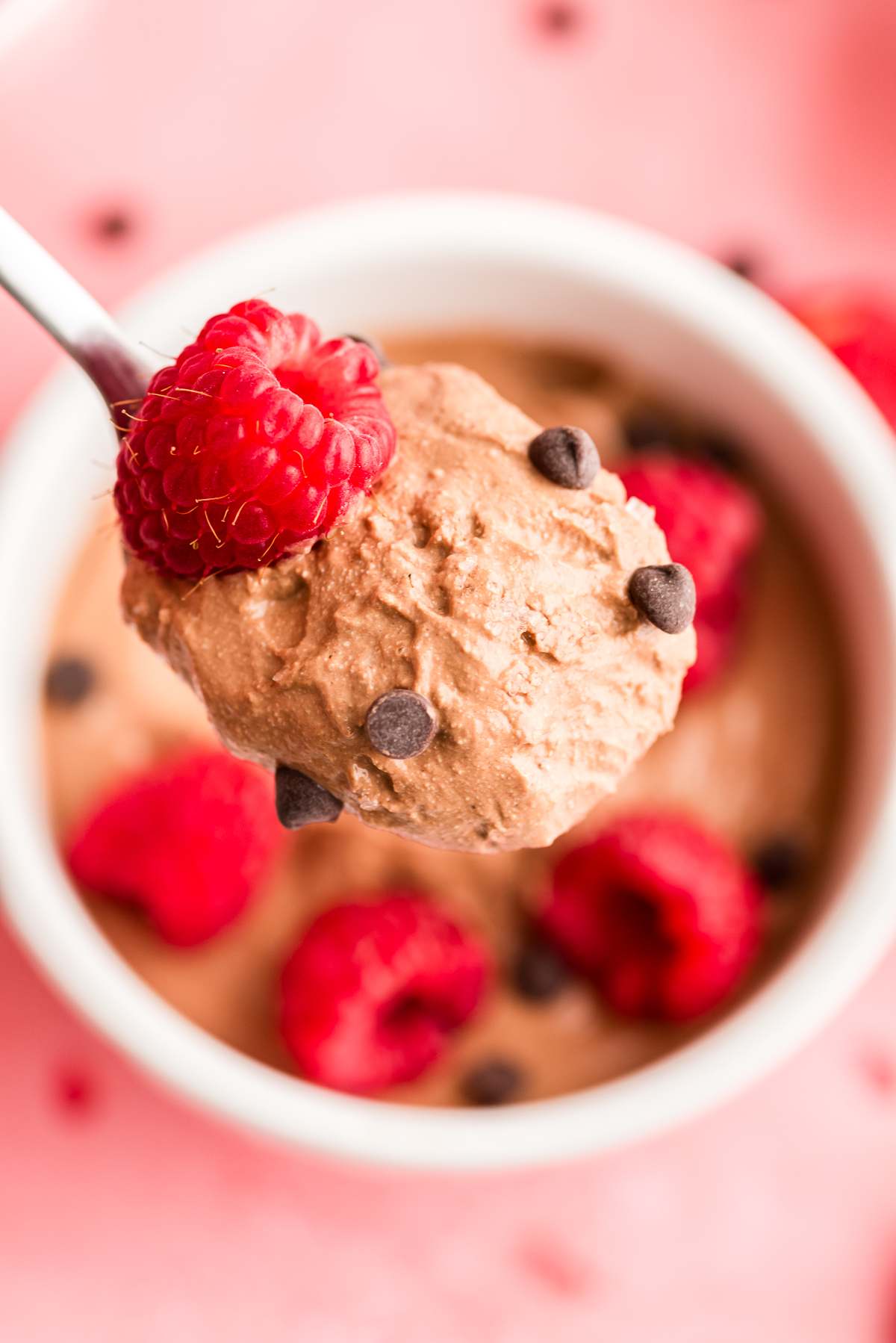 Large spoonful of chocolate cottage cheese mousse being lifted out of a bowl with raspberries on top.