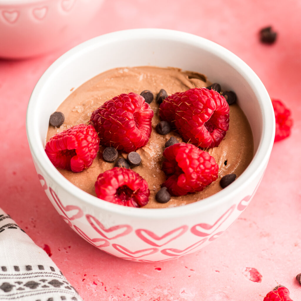 Bowl filled with chocolate cottage cheese mousse with raspberries and chocolate chips on top.