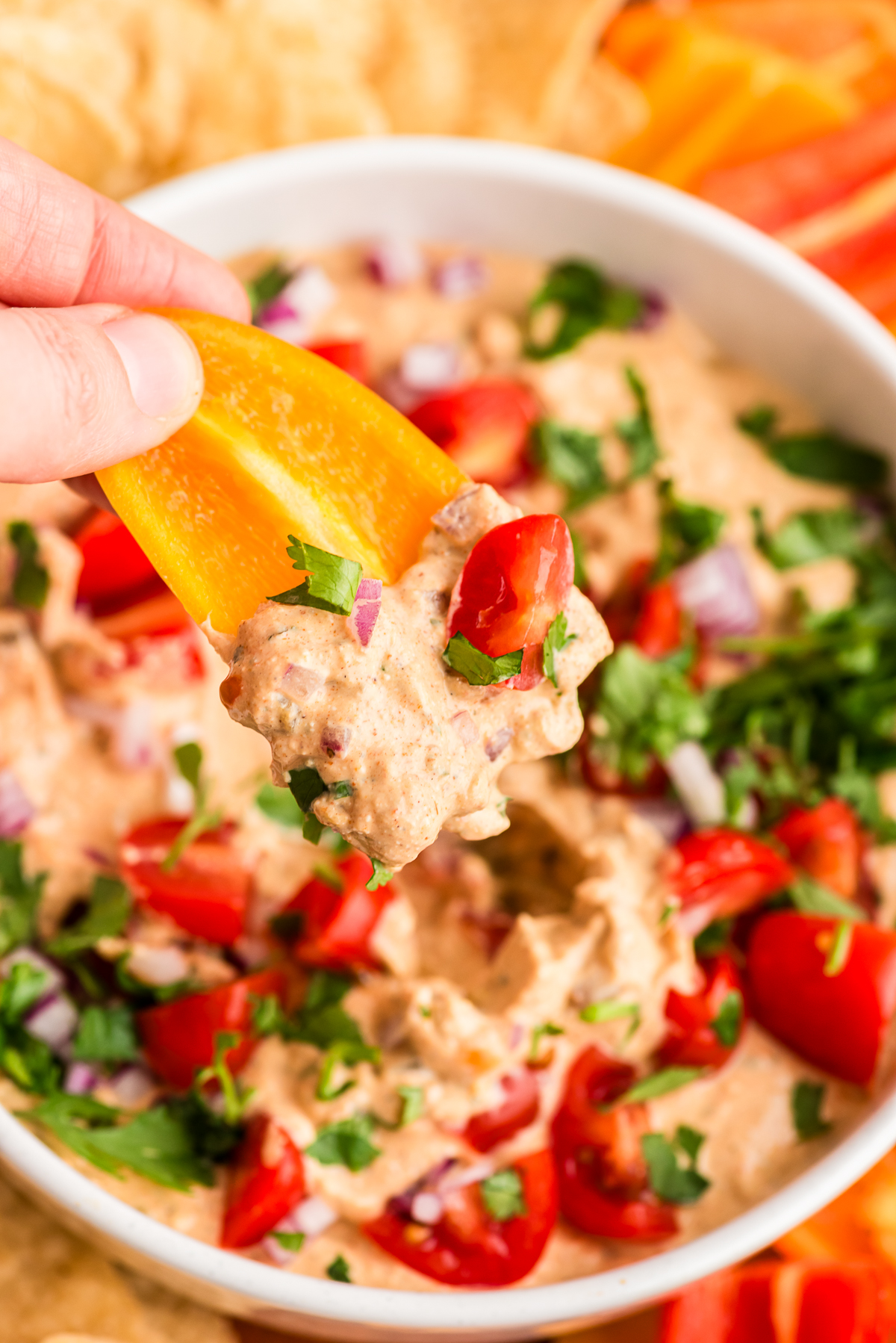 Hand dipping a bell pepper into cottage cheese taco dip.