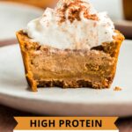 Protein mini pumpkin cheesecakes on white plate with whipped cream and pumpkin pie spice.