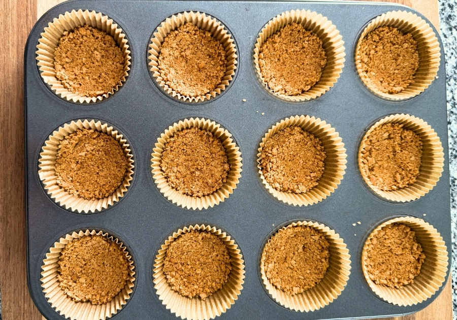 Graham cracker crust in muffin tin before pressing it down.
