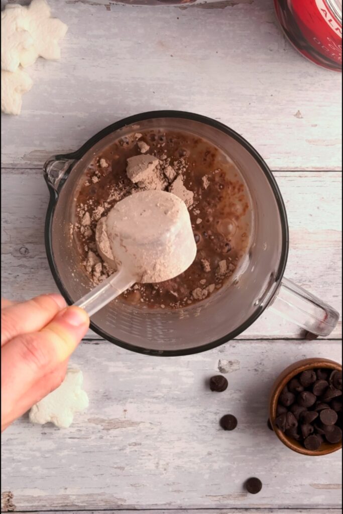 Scoop of protein powder being added to glass.