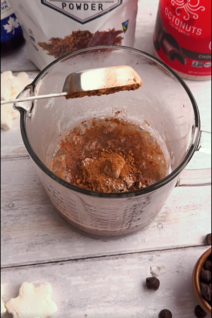 Cacao powder being dropped into glass with protein powder.