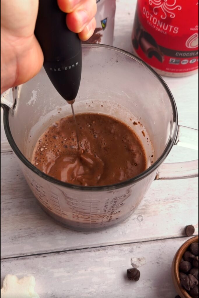 Frother mixing chocolate mixture in glass measuring cup.
