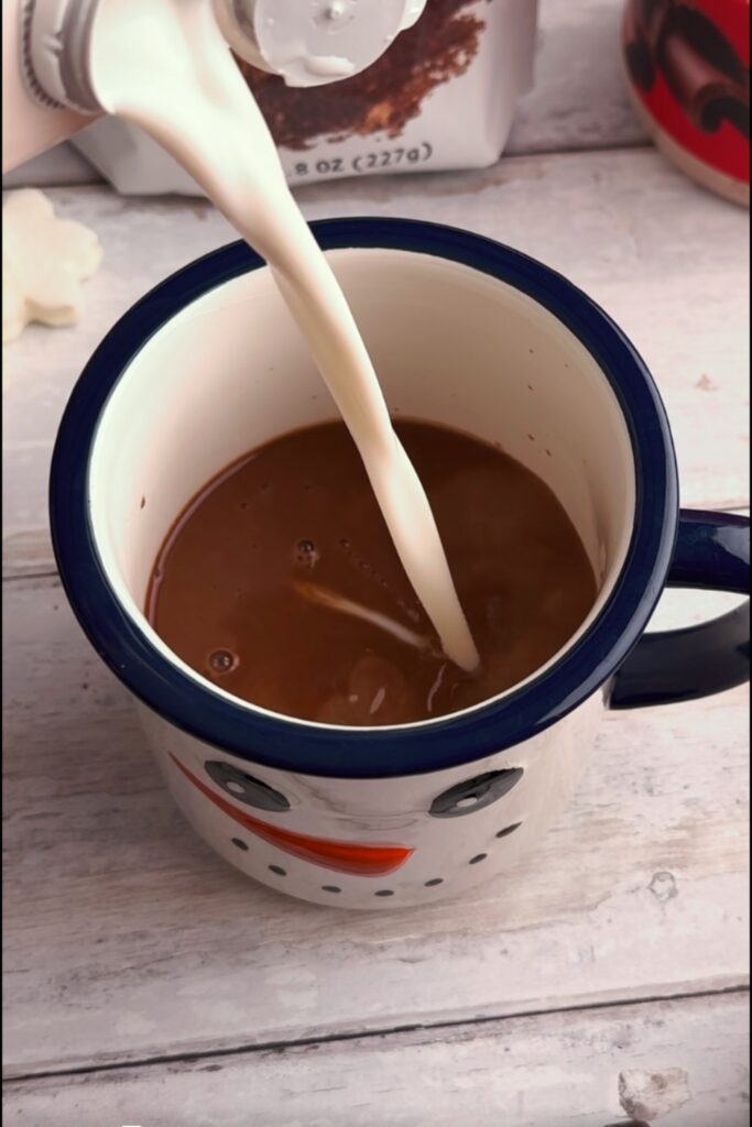 Milk being added to chocolate mixture in mug.