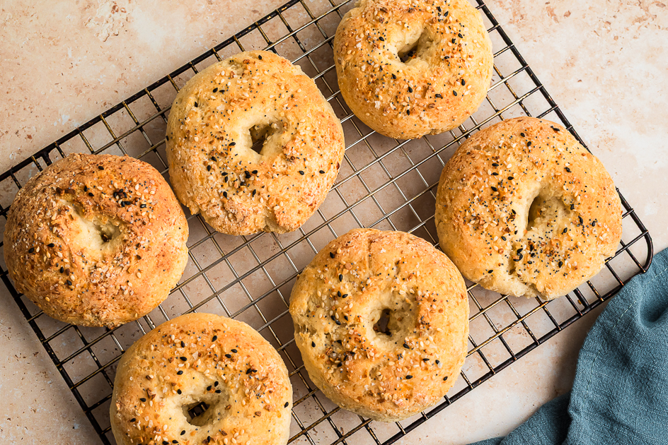 Six gluten free cottage cheese bagels on a wire cooling rack, blue napkin on the side. 
