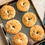Six gluten free cottage cheese bagels on a baking sheet.
