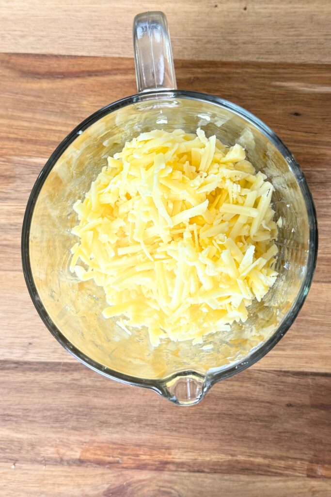 Shredded cheddar cheese in a glass measuring cup.