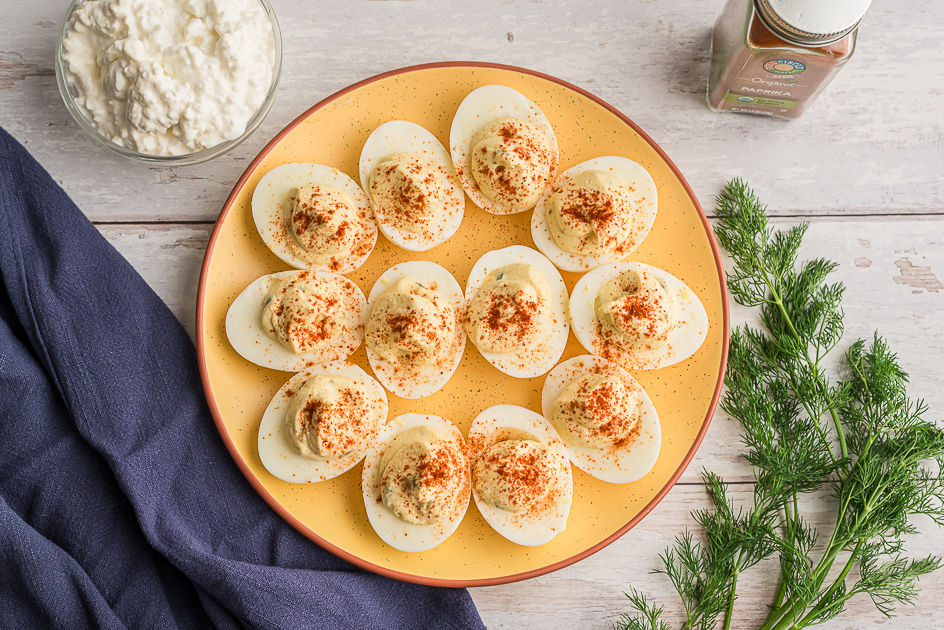 Deviled eggs with cottage cheese on a yellow plate with dill on the side. 