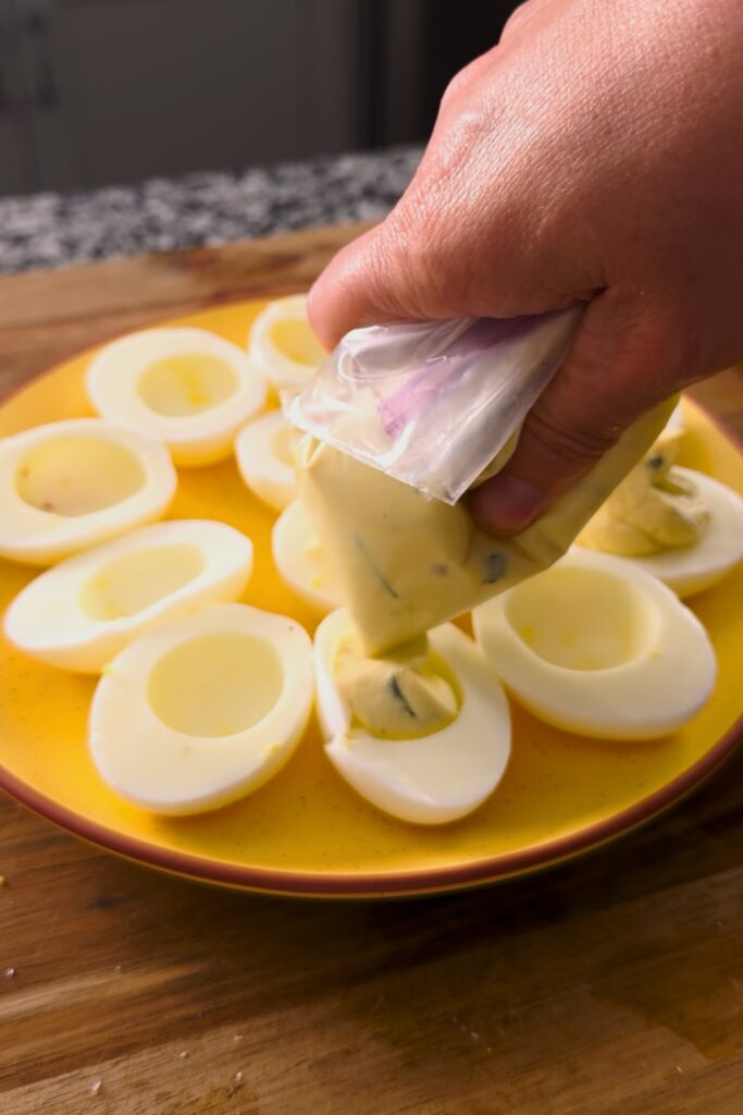 Hand squeezing egg mixture into egg halves.
