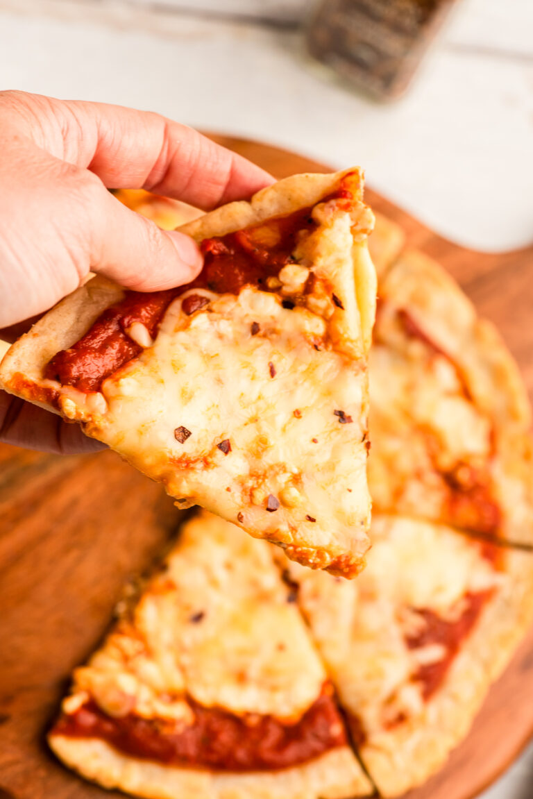 Hand holding a slice of cottage cheese pizza.